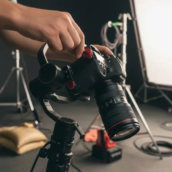 A person precisely balancing a heavy DSLR and zoom lens on a gimbal, adjusting its axes.